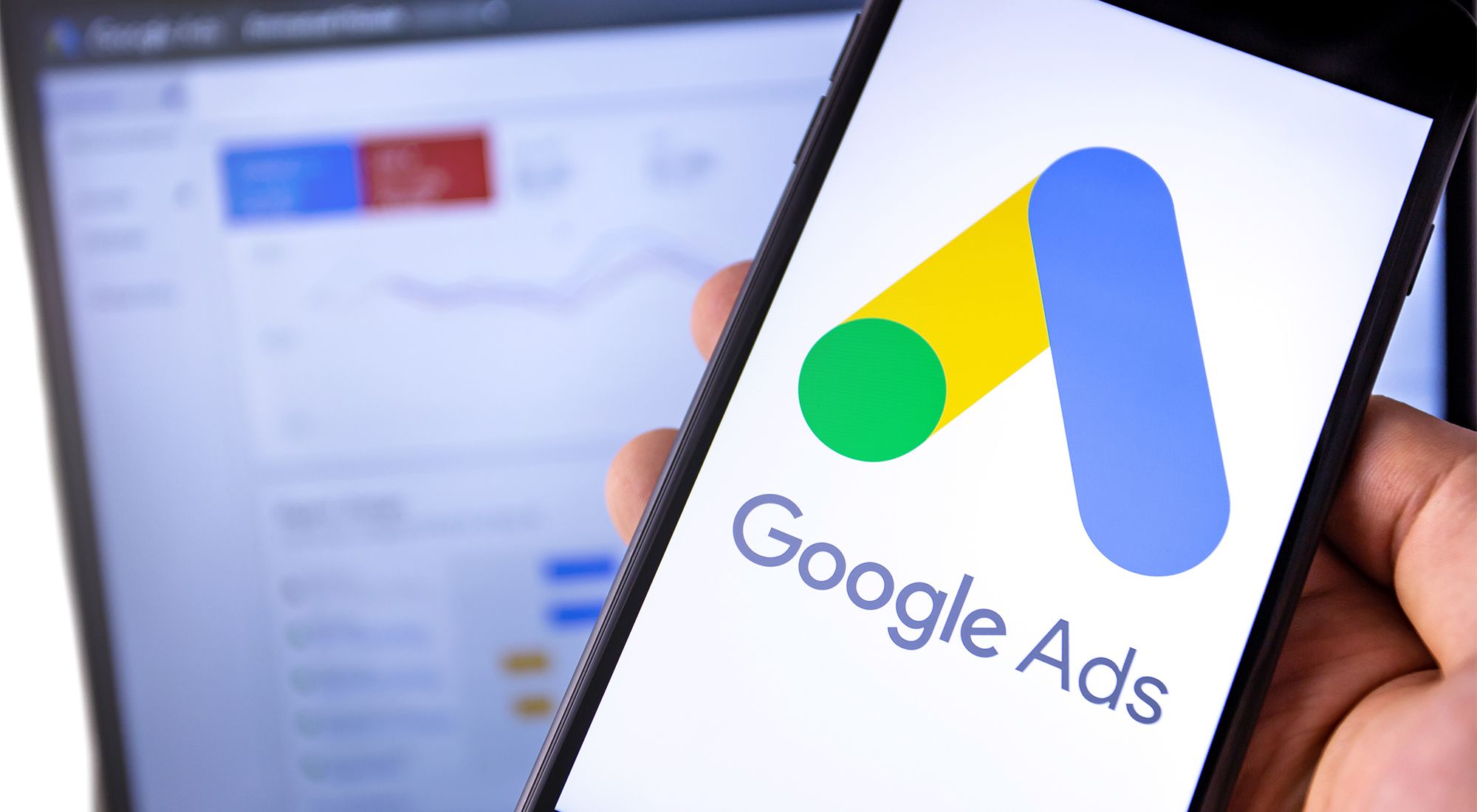 Google Ads logo on a phone with a laptop in background by Moonlane Media